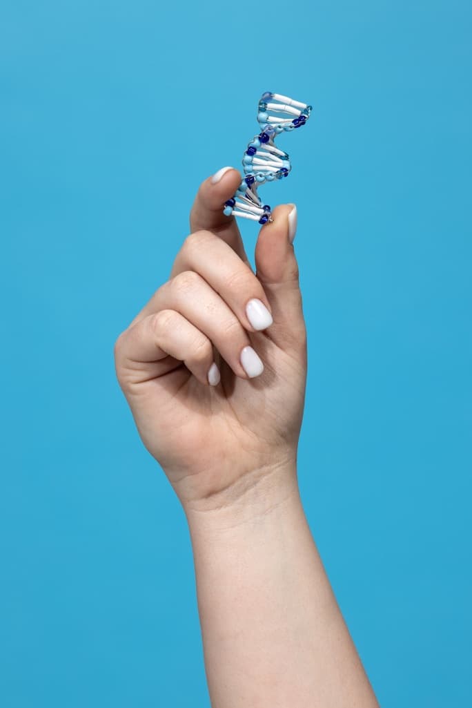 A hand holding a small beaded DNA double helix against a blue background